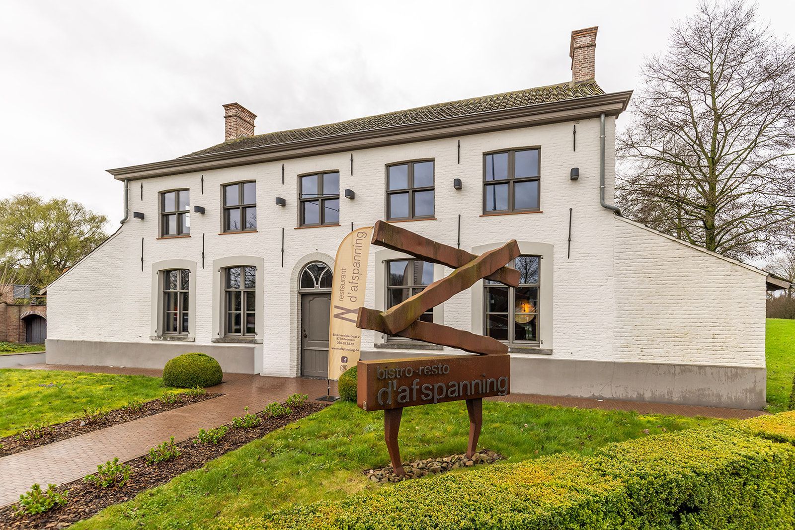 A white two-story brick building with a dark sculpture in the front yard featuring the text