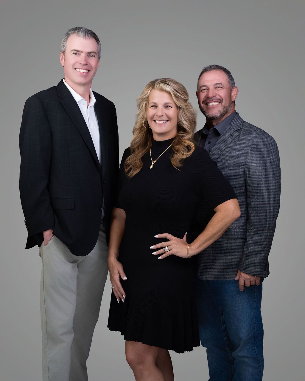 Three people posing in studio attire against a gray background