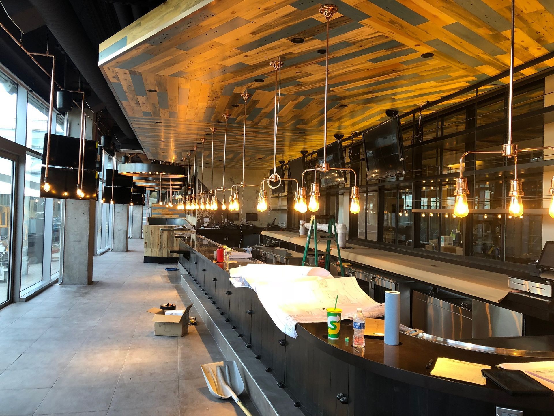 A long bar in a restaurant with lots of lights hanging from the ceiling.