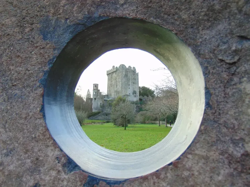 A view of Blarney Castle in Ireland seen through a circular hole in a stone wall.