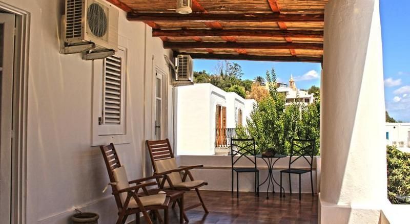 Patio ombreggiato con sedie e tavolo in legno, pareti bianche e vista sull'oceano sotto un tetto di tegole.