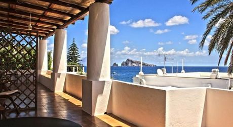 Terrazza coperta sul mare con colonne, pareti bianche e vista sull'oceano sotto un cielo azzurro e soleggiato.