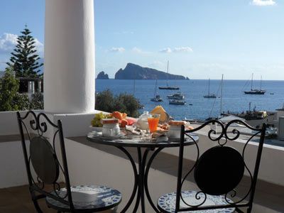 Tavolino apparecchiato in un caffè sul mare per la colazione, con vista sulle barche e sull'oceano blu sotto un cielo limpido.