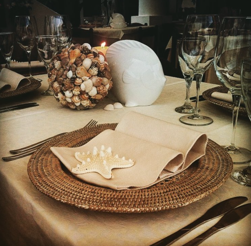 Elegante apparecchiatura della tavola con tovaglietta intrecciata, tovagliolo piegato, decorazione a conchiglia e candela.