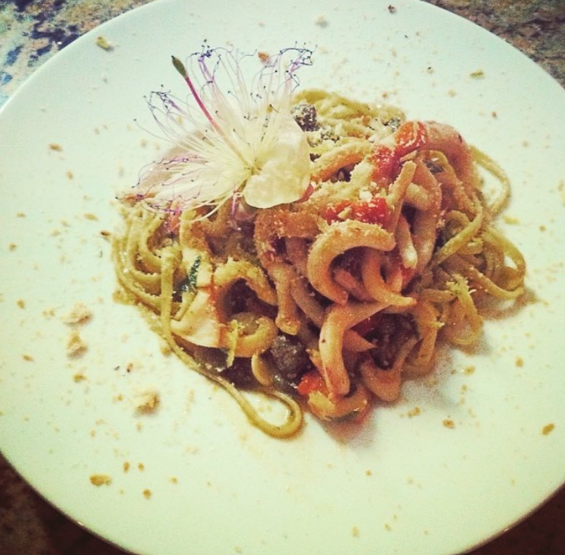 Spaghetti conditi con sugo e formaggio grattugiato su un piatto bianco, decorati con un fiore.
