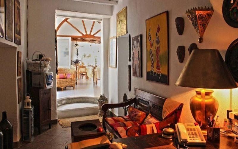 Accogliente soggiorno con divano rosso, lampada a sospensione dai colori caldi, quadri alle pareti e porta aperta su un luminoso patio.