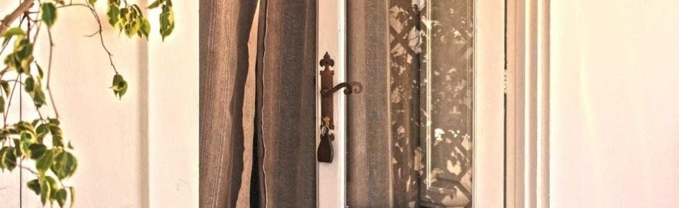 Una finestra soleggiata con tende trasparenti e una pianta appesa accanto a un drappeggio decorato