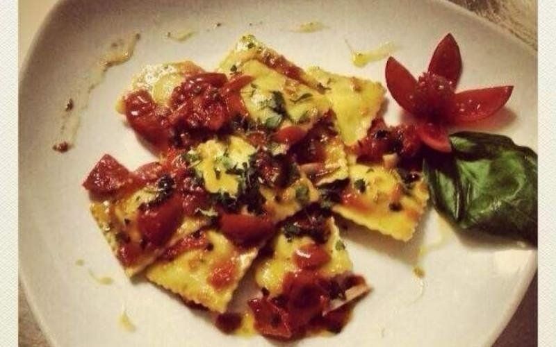 Pasta al sugo di pomodoro ed erbe aromatiche, guarnita con una foglia di basilico e un fiore di pomodoro su un piatto bianco.