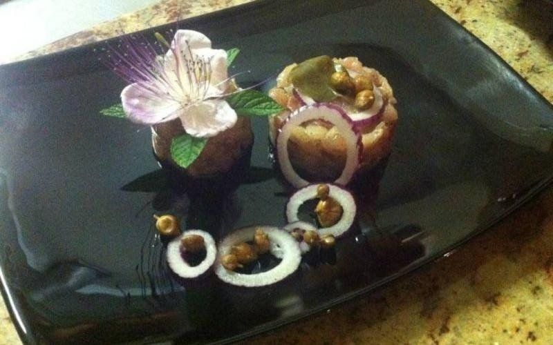 Vassoio nero con una piccola composizione di fiori e snack bianchi a forma di anello su una tovaglia decorata.
