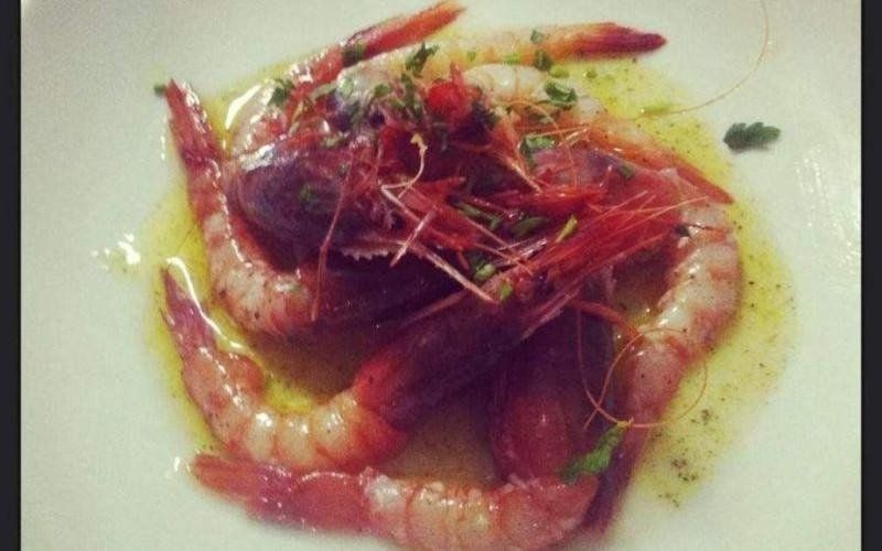 Piatto di frutti di mare con gamberi, erbe aromatiche e salsa su sfondo chiaro.