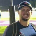 A man wearing a baseball cap and sunglasses is smiling for the camera.