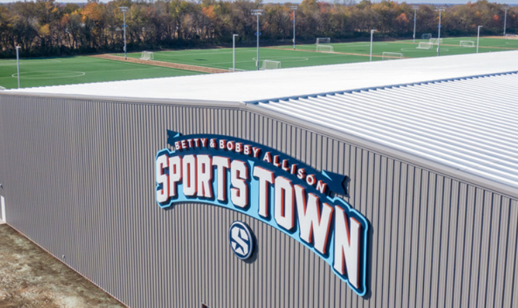 An aerial view of a sports town building with a baseball field in the background.
