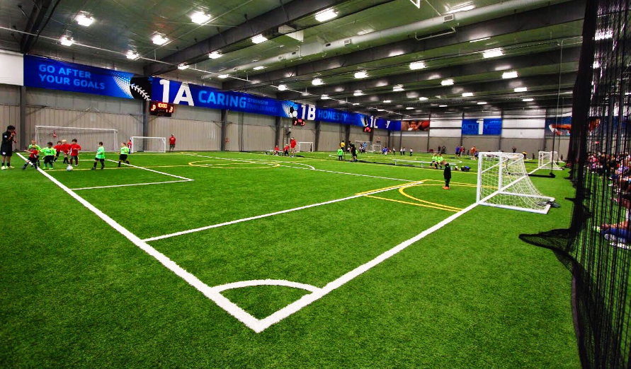 A group of children are playing soccer in an indoor stadium.