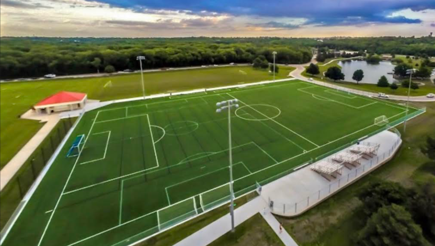 An aerial view of a soccer field surrounded by trees and a lake.
