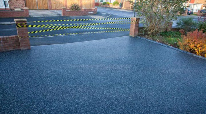 Blue resin driveway leading to a gated entrance with yellow-and-black warning stripes and brick pillars