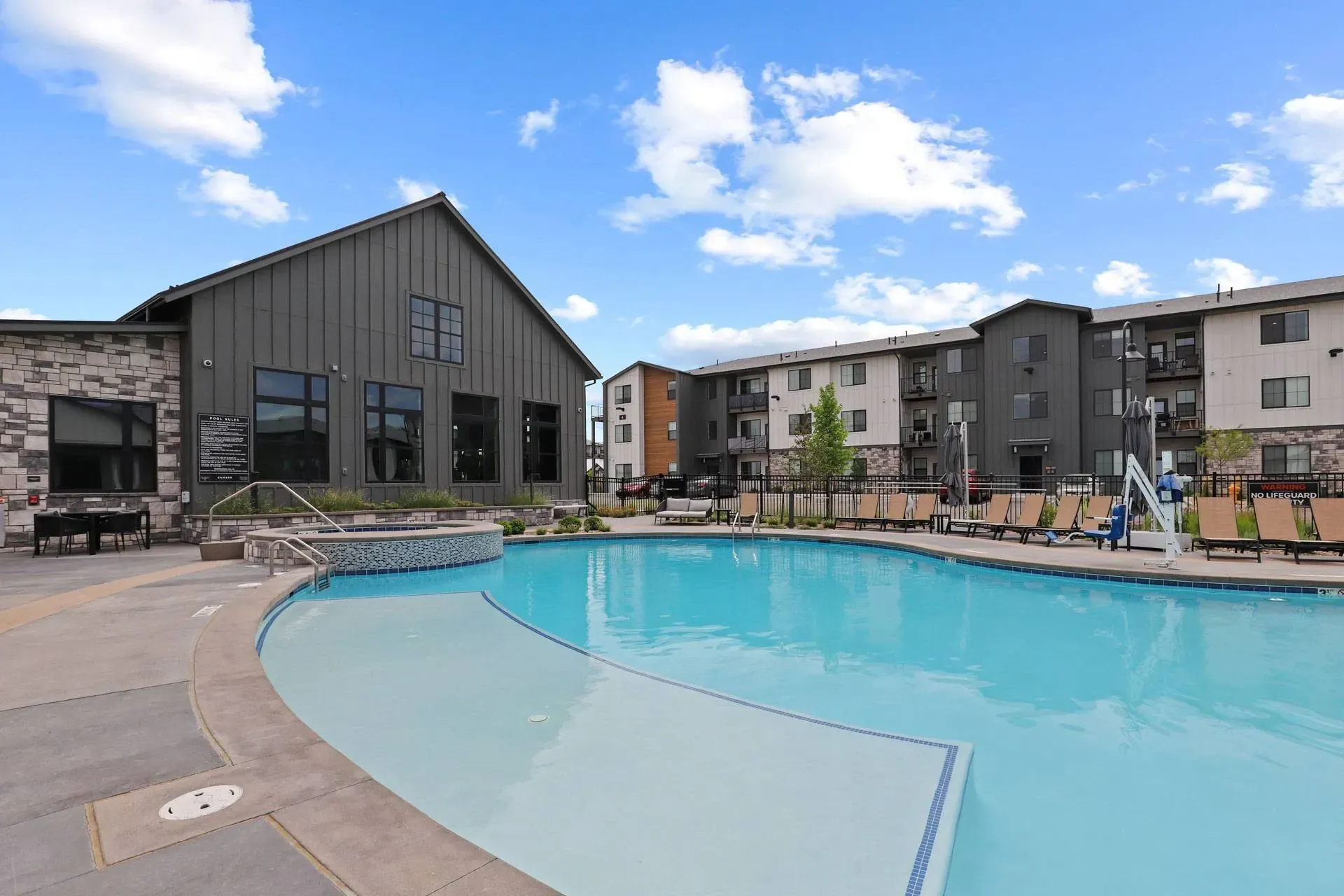 Outdoor swimming pool and hot tub with lounge chairs and apartment buildings in the background.