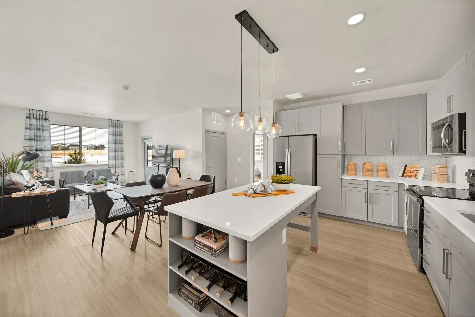 Open concept living and dining area with a modern kitchen featuring grey cabinets and a large island.