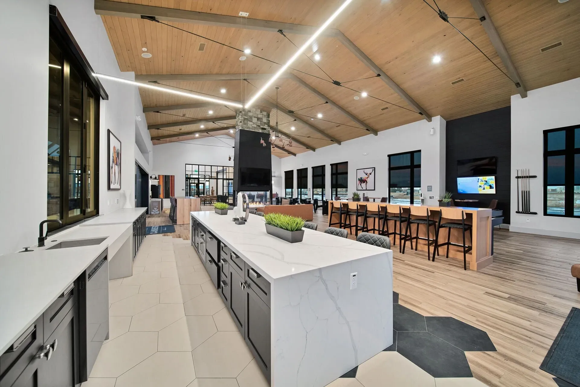 Modern apartment community lounge with kitchen island, bar seating, fireplace, and billiards cues.
