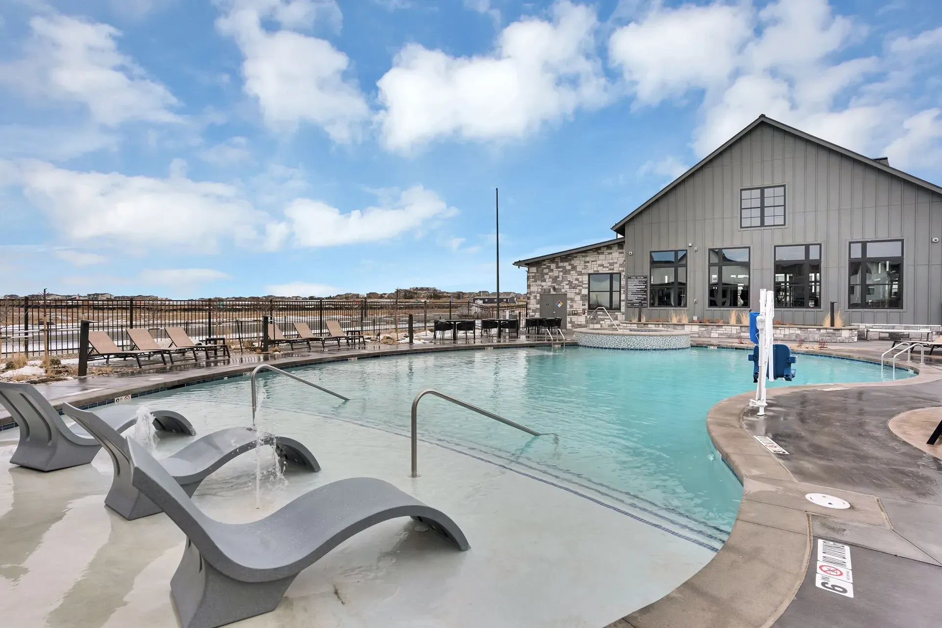 Outdoor swimming pool with lounge chairs and a hot tub next to a modern building.