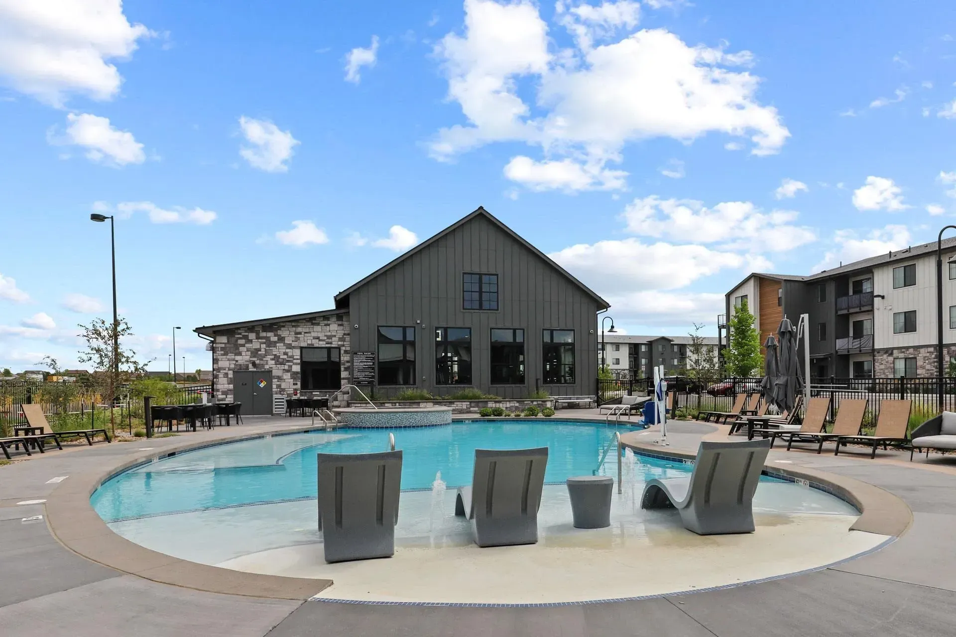 Resort-style swimming pool with lounge chairs and modern building in the background.