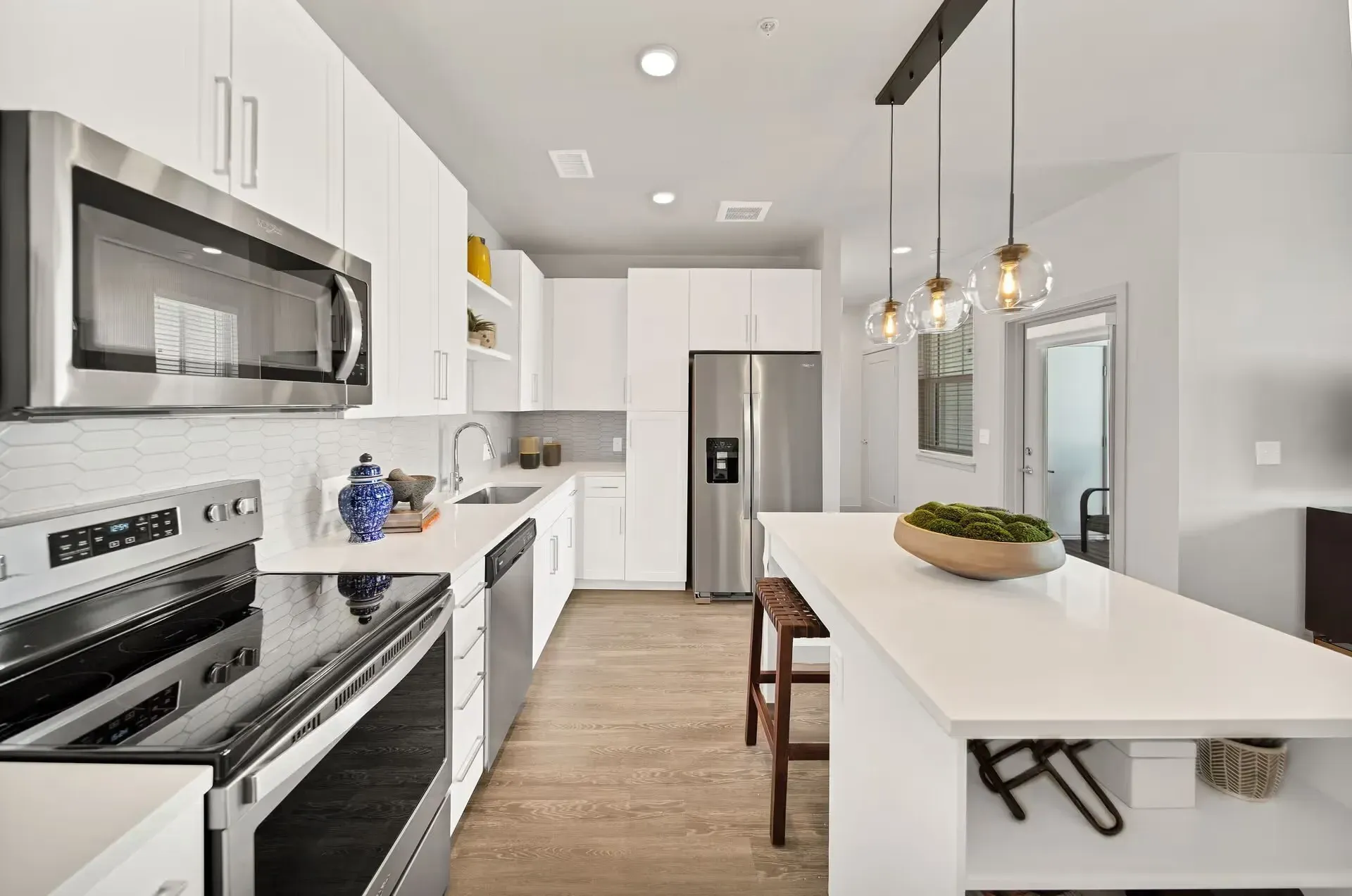 Modern white kitchen with stainless appliances, island seating, and pendant lights
