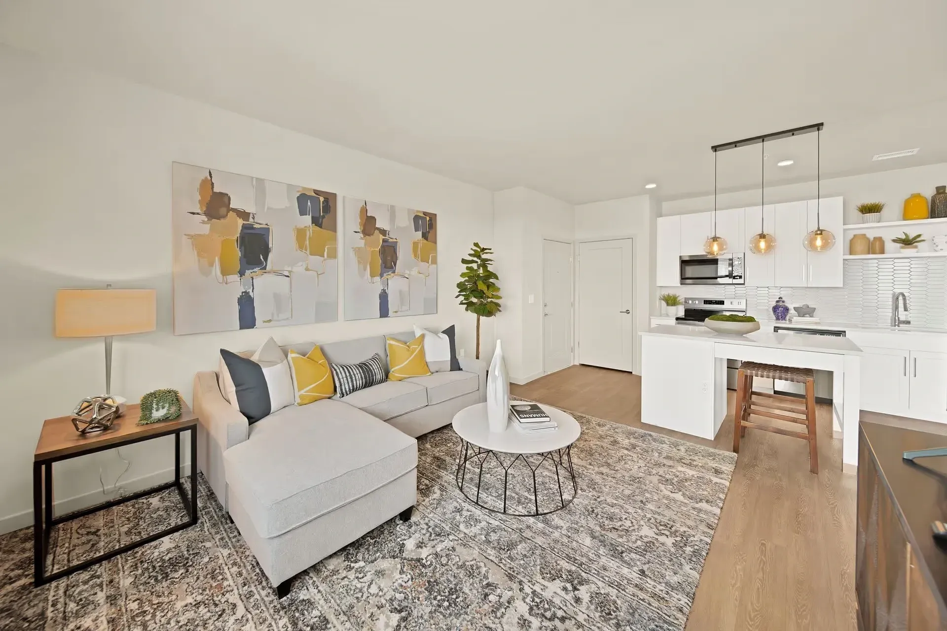 Bright modern living room and kitchen with gray sofa, yellow accents, rug, and island seating
