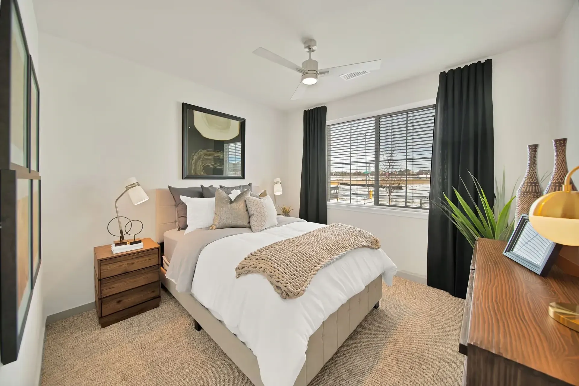 Bright bedroom with a white bed, dark curtains, bedside table, and large window view