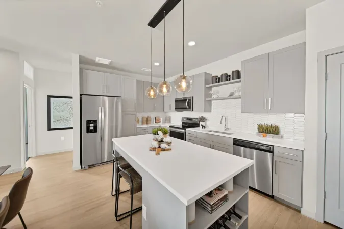 Modern kitchen with white island, gray cabinets, stainless appliances, and pendant lights