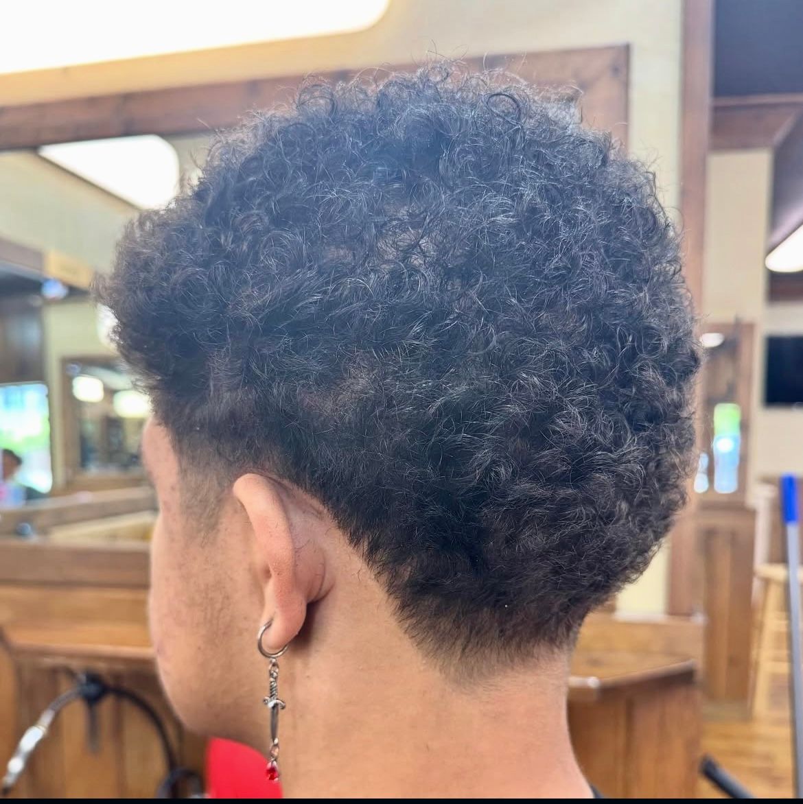 Person with dark, textured hair and a faded haircut in a barbershop.