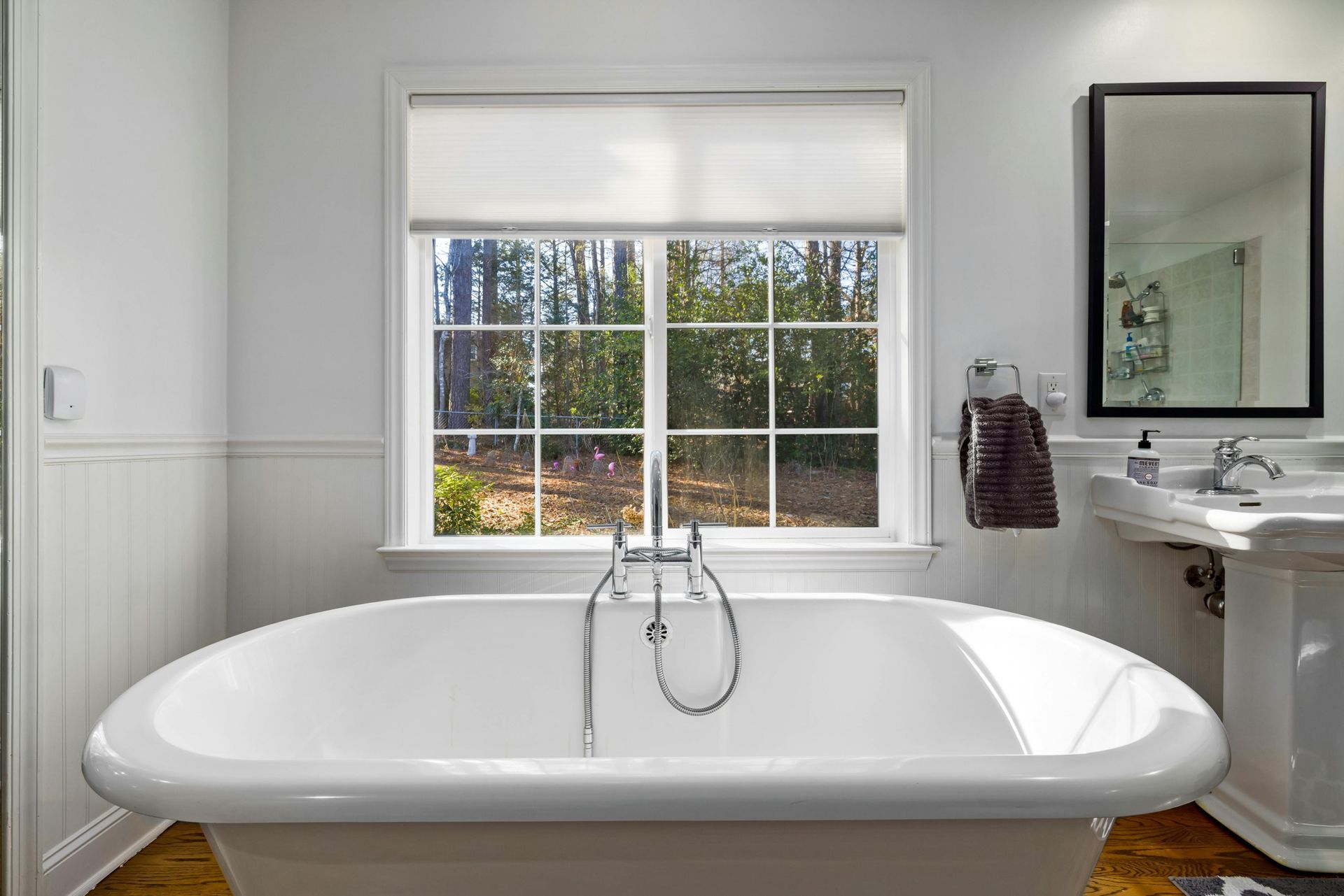 A bathroom with a claw foot tub , sink , mirror and window.