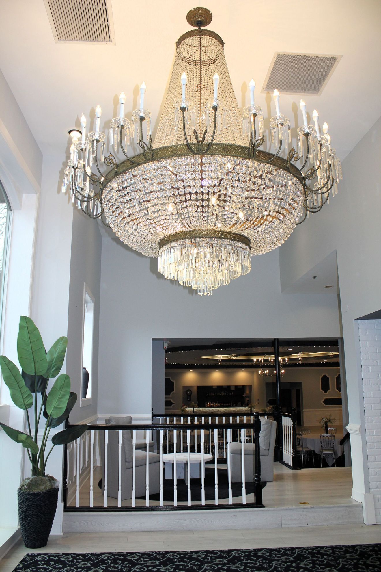 Grand chandelier in a modern lobby with white walls, railing, and potted plant below