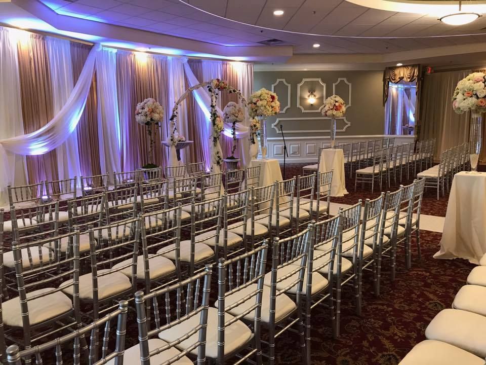 Elegant banquet hall with white chairs, mirrored aisle, floral arrangements, and purple accent lighting