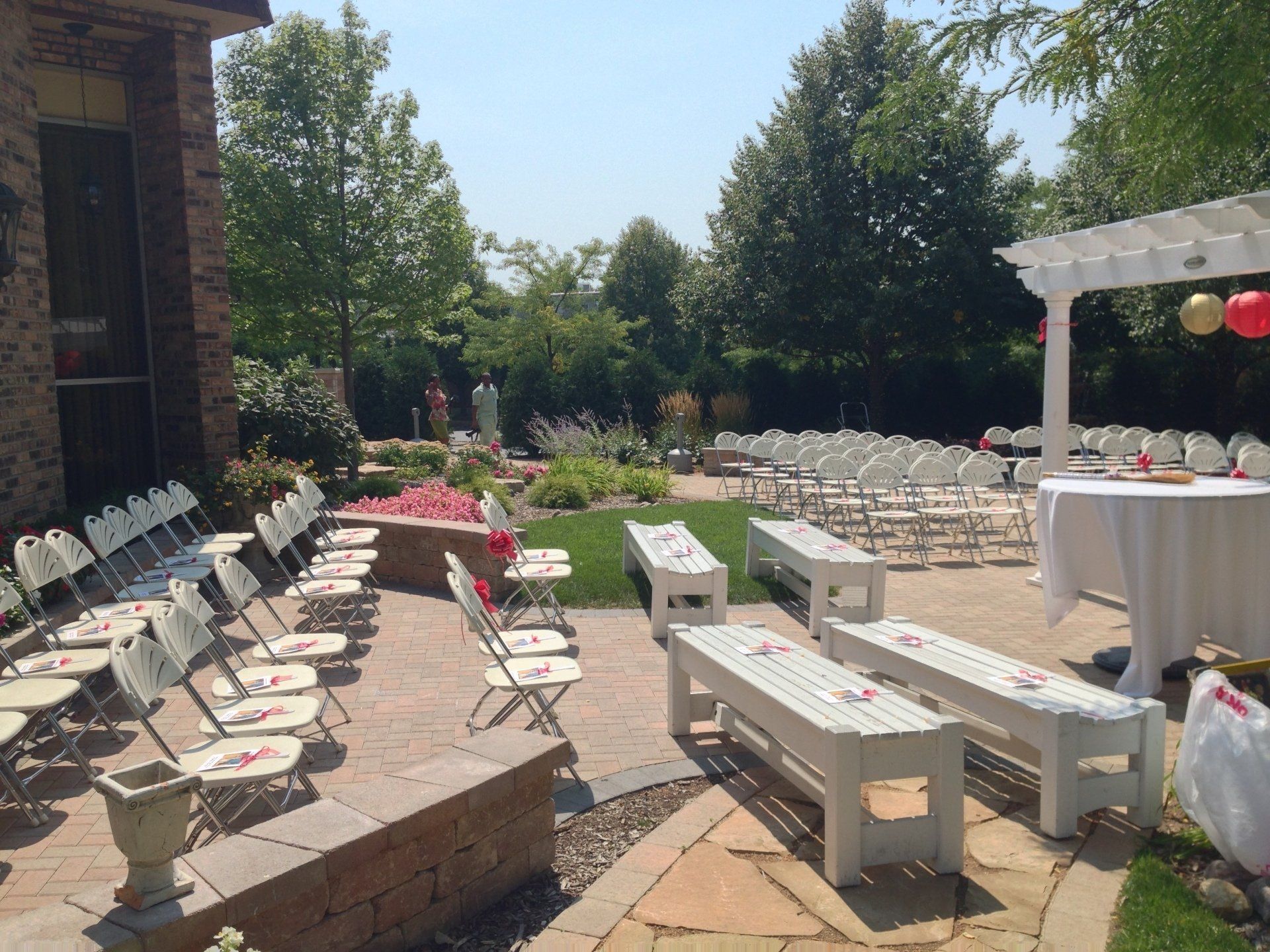 Outdoor event setup with white chairs, long benches, and tables on a sunny patio