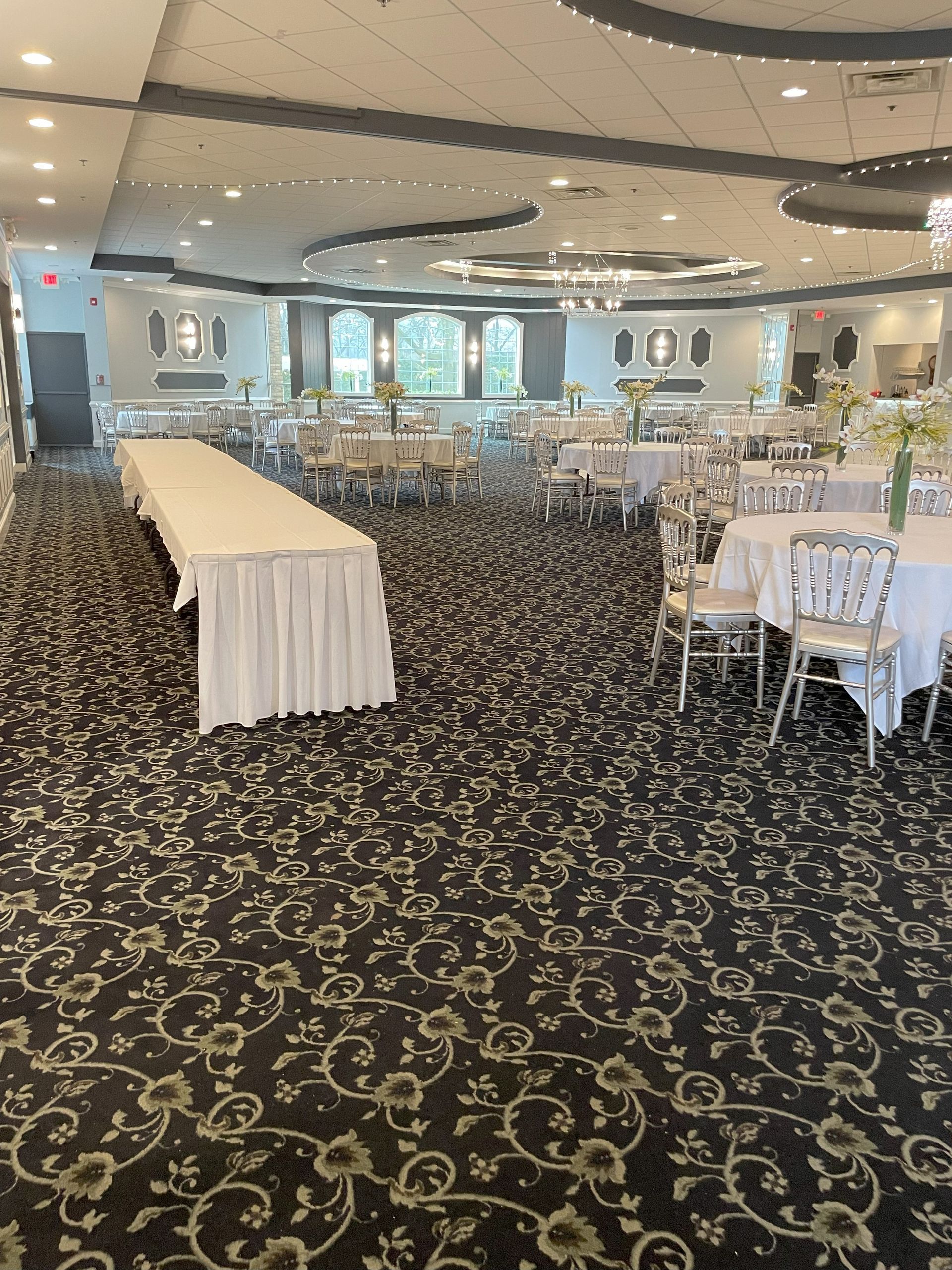 Elegant banquet hall with long tables, white chairs, and patterned carpet under mirrored ceiling lights