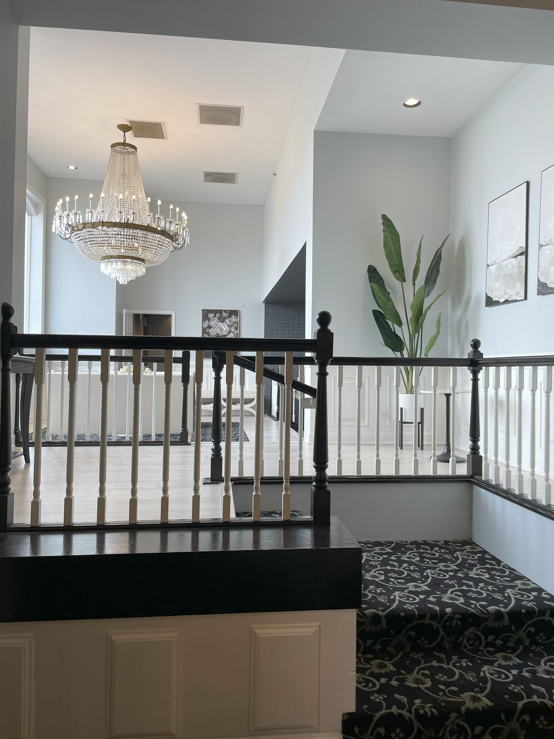 Elegant home staircase with black railing, chandelier, and potted plant in a bright foyer