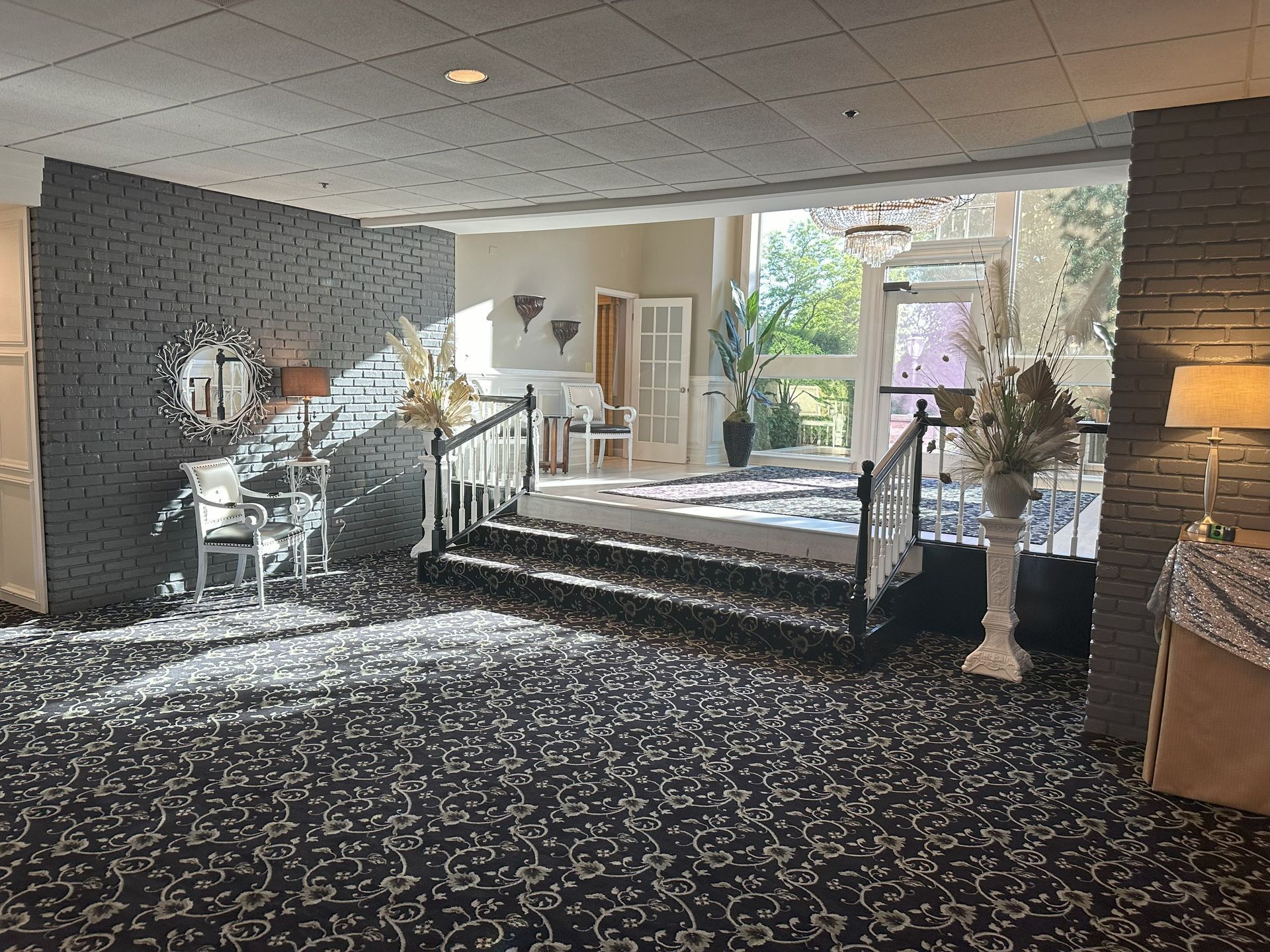 Hotel lobby with carpeted seating area, decorative plants, and stairs leading to a bright doorway