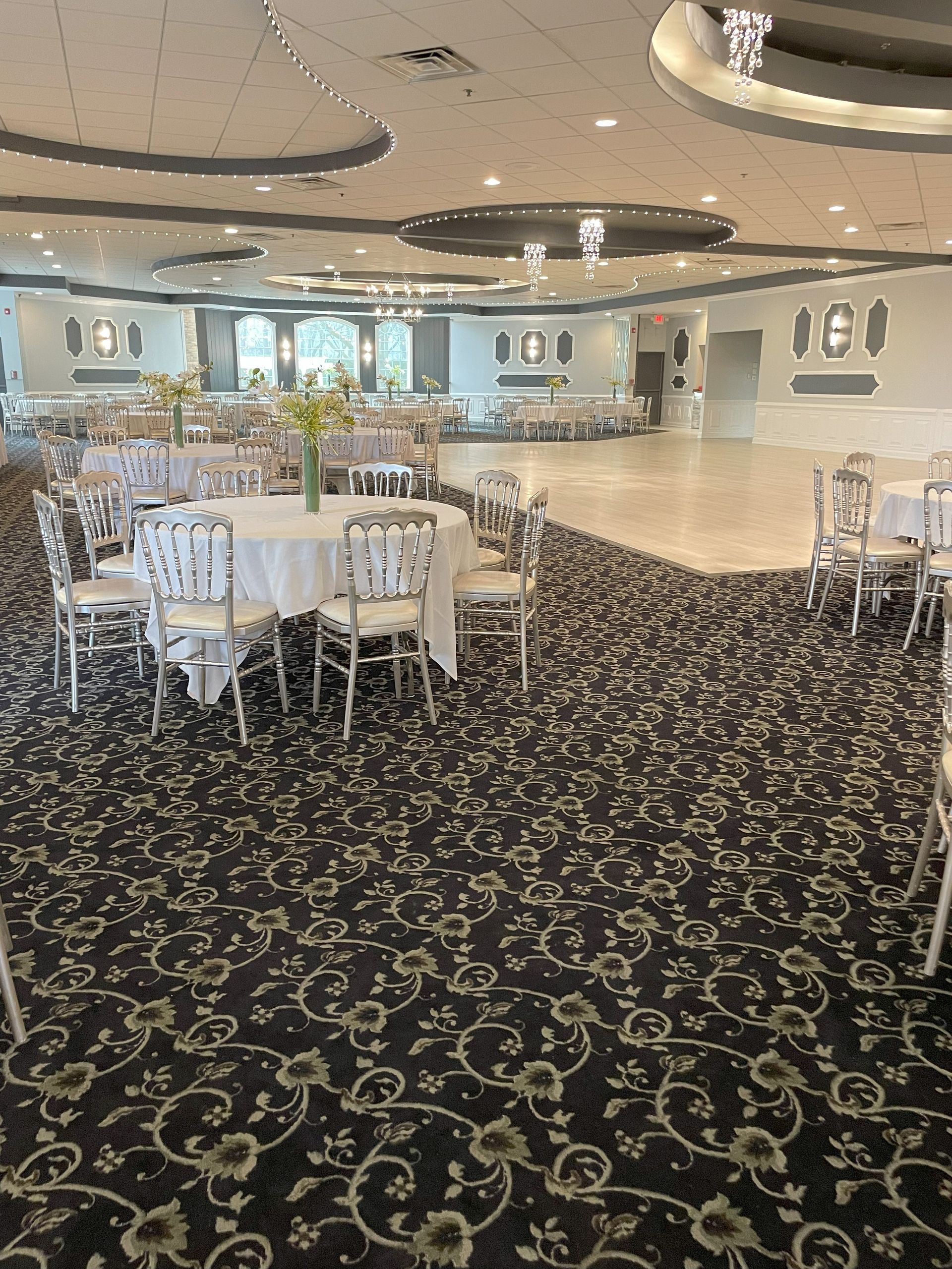 Elegant banquet hall with round tables, white chairs, and patterned carpet under soft ceiling lights