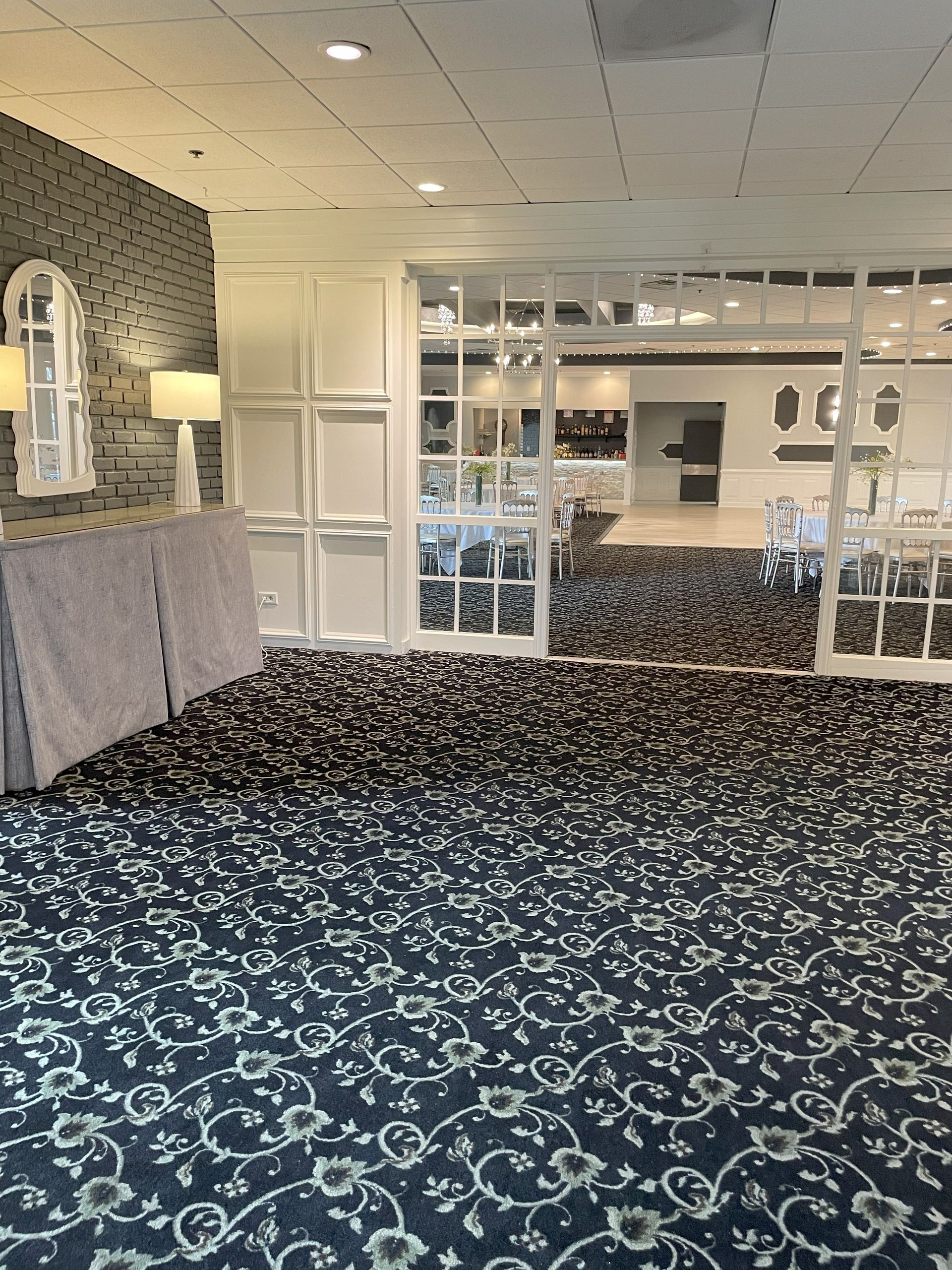 Empty lobby with patterned blue carpet, glass partitions, and a reception desk area.