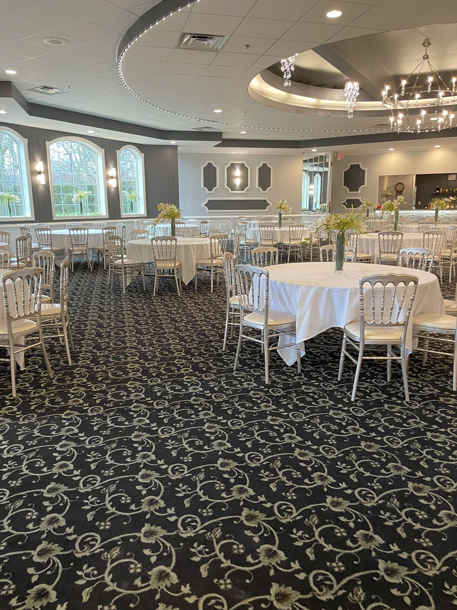 Elegant banquet hall with white-clothed tables, ornate chairs, chandeliers, and patterned carpet