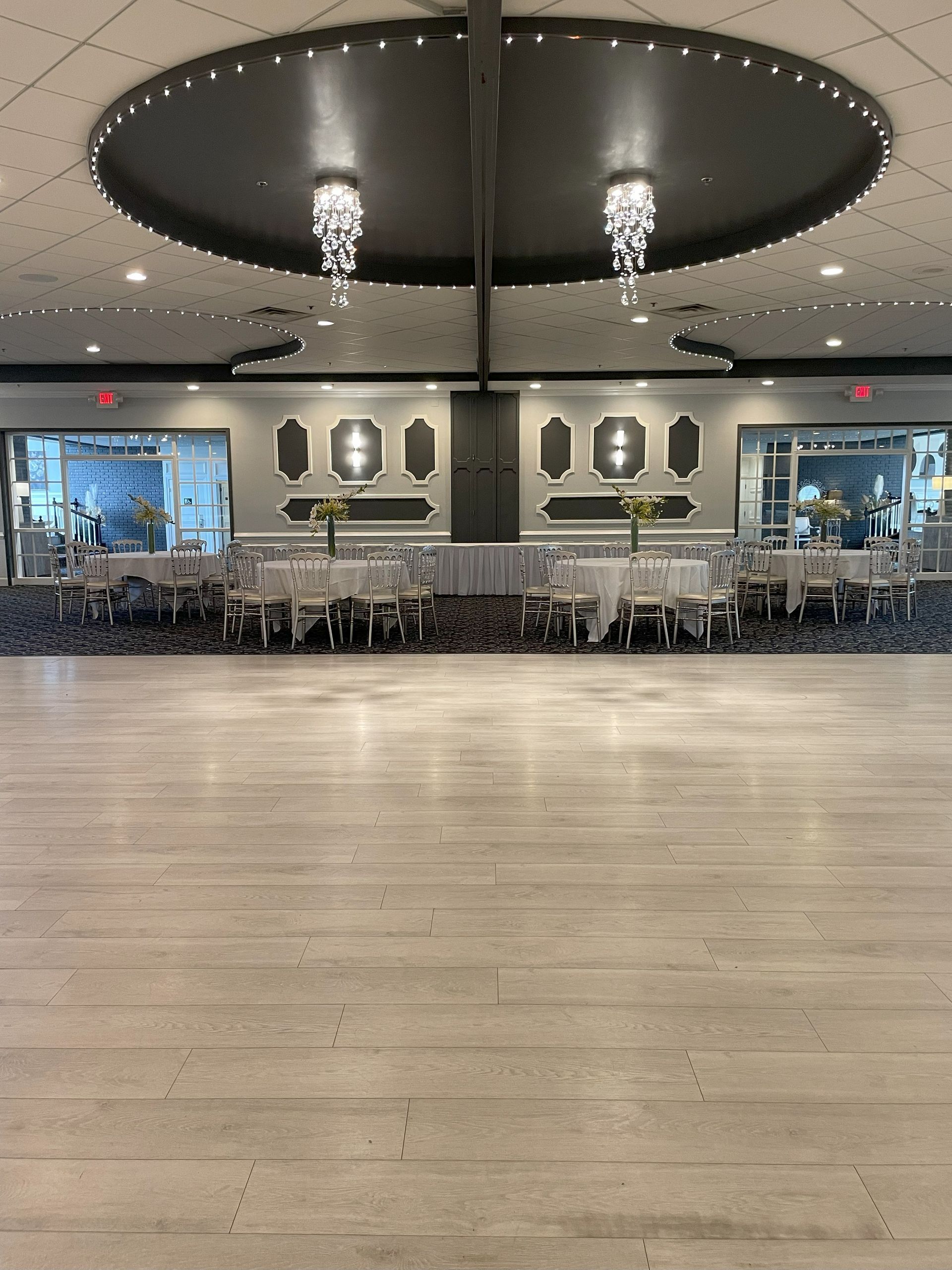 Modern lobby with wood floor, black oval ceiling lights, and rows of chairs along mirrored walls