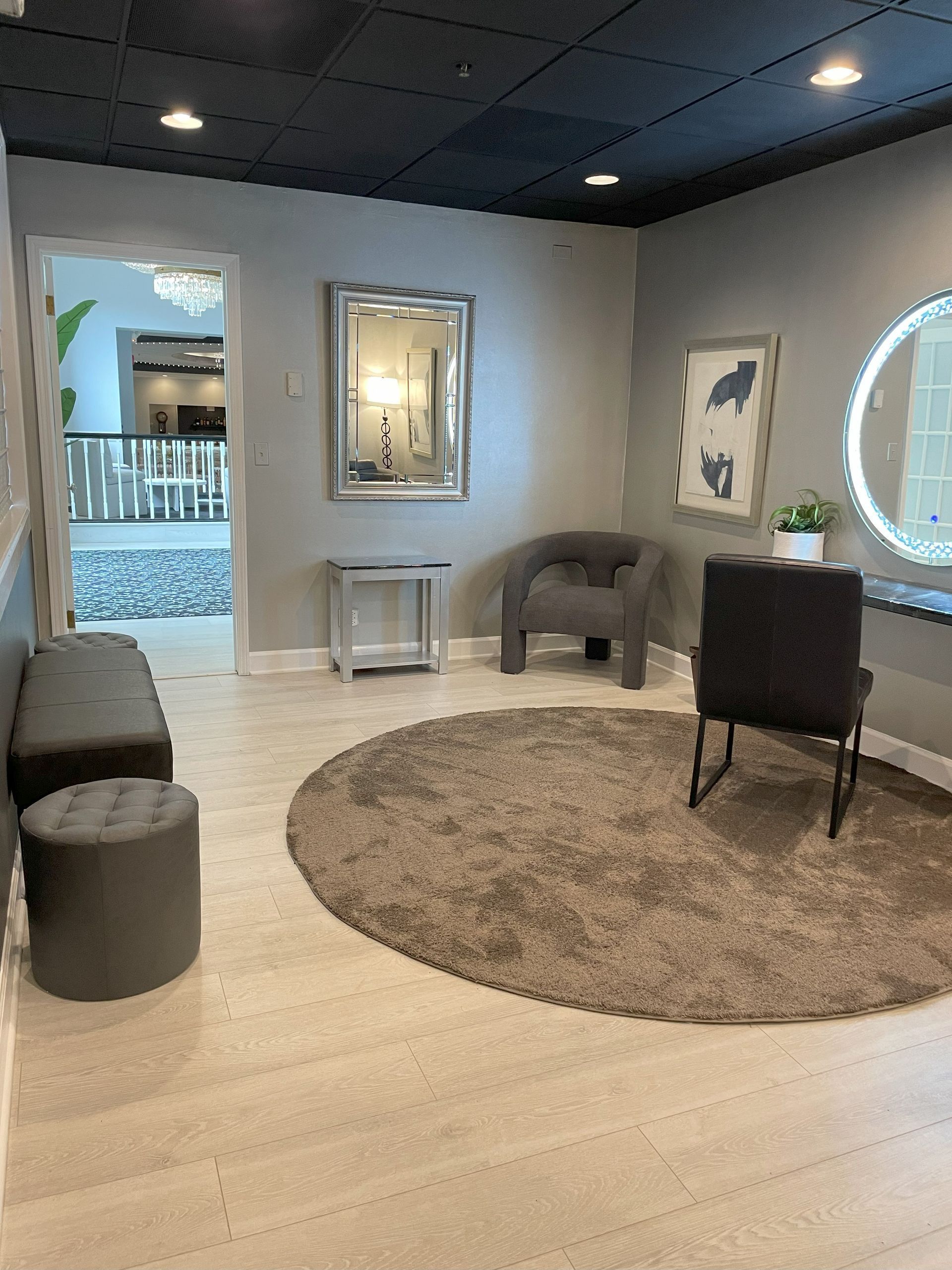 Modern lounge with round rug, gray chairs, vanity mirror, and large window overlooking water