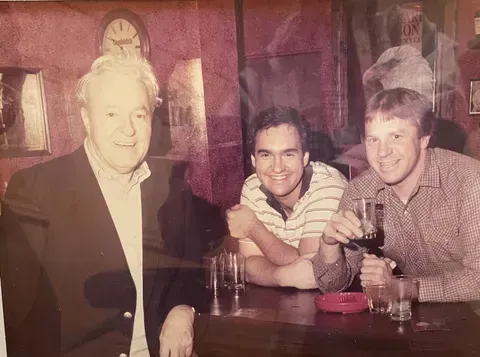 Three people smiling at a bar, with drinks on the counter and warm, dim lighting.