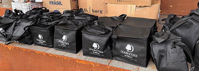 Sacos de entrega pretos com um logotipo branco dispostos em uma prateleira em frente a caixas de papelão.
