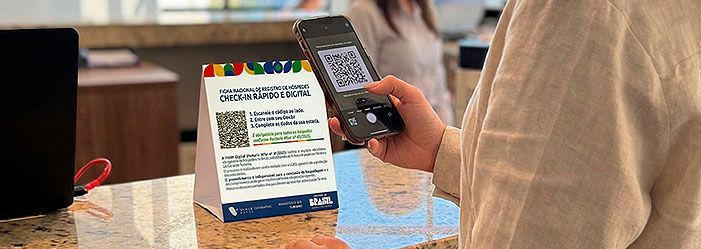 Uma pessoa usa um smartphone para escanear um código QR exibido em uma pequena placa sobre uma mesa em um balcão.