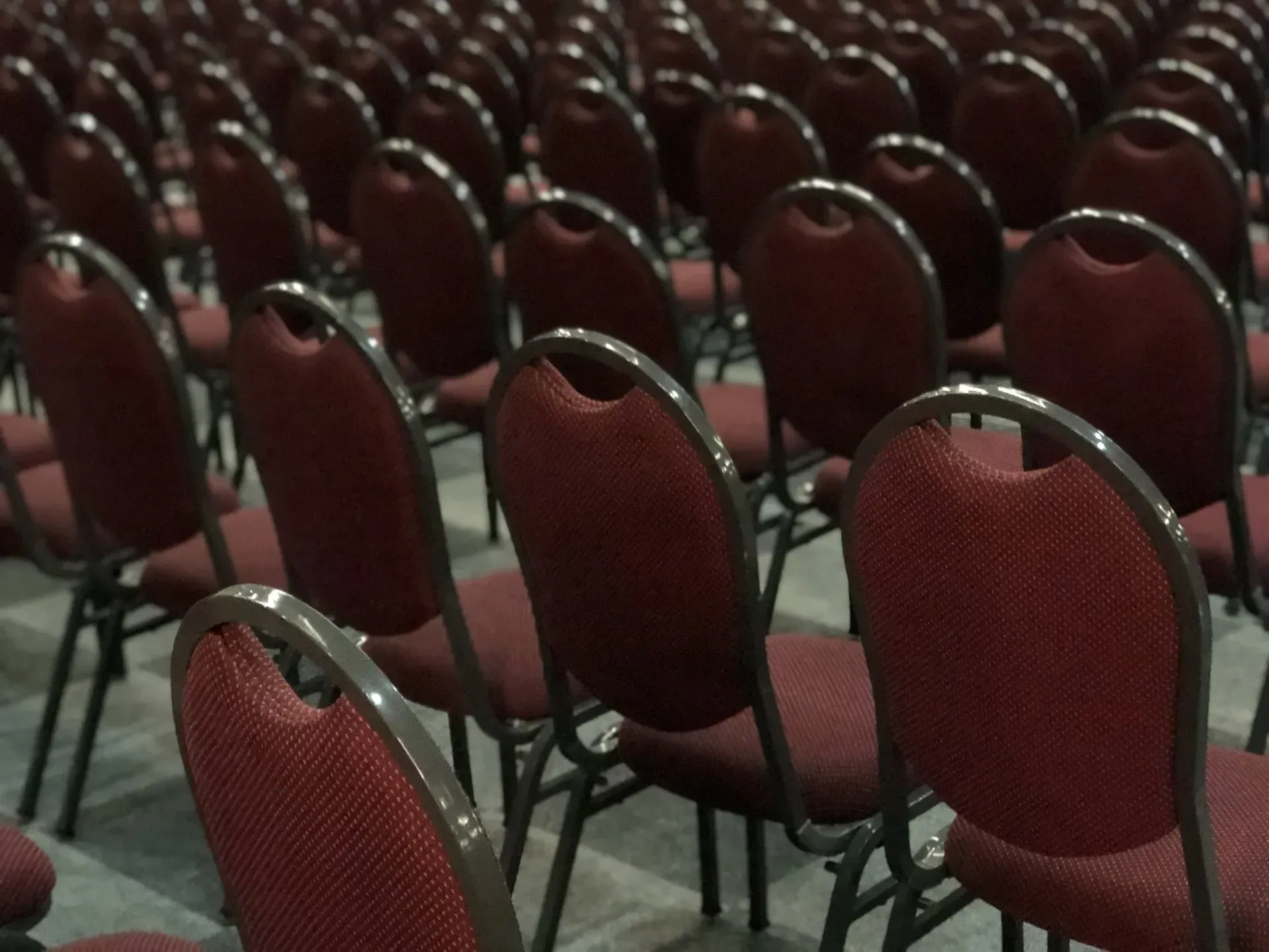 Fileiras de cadeiras estofadas vermelhas em um grande auditório, prontas para um evento.