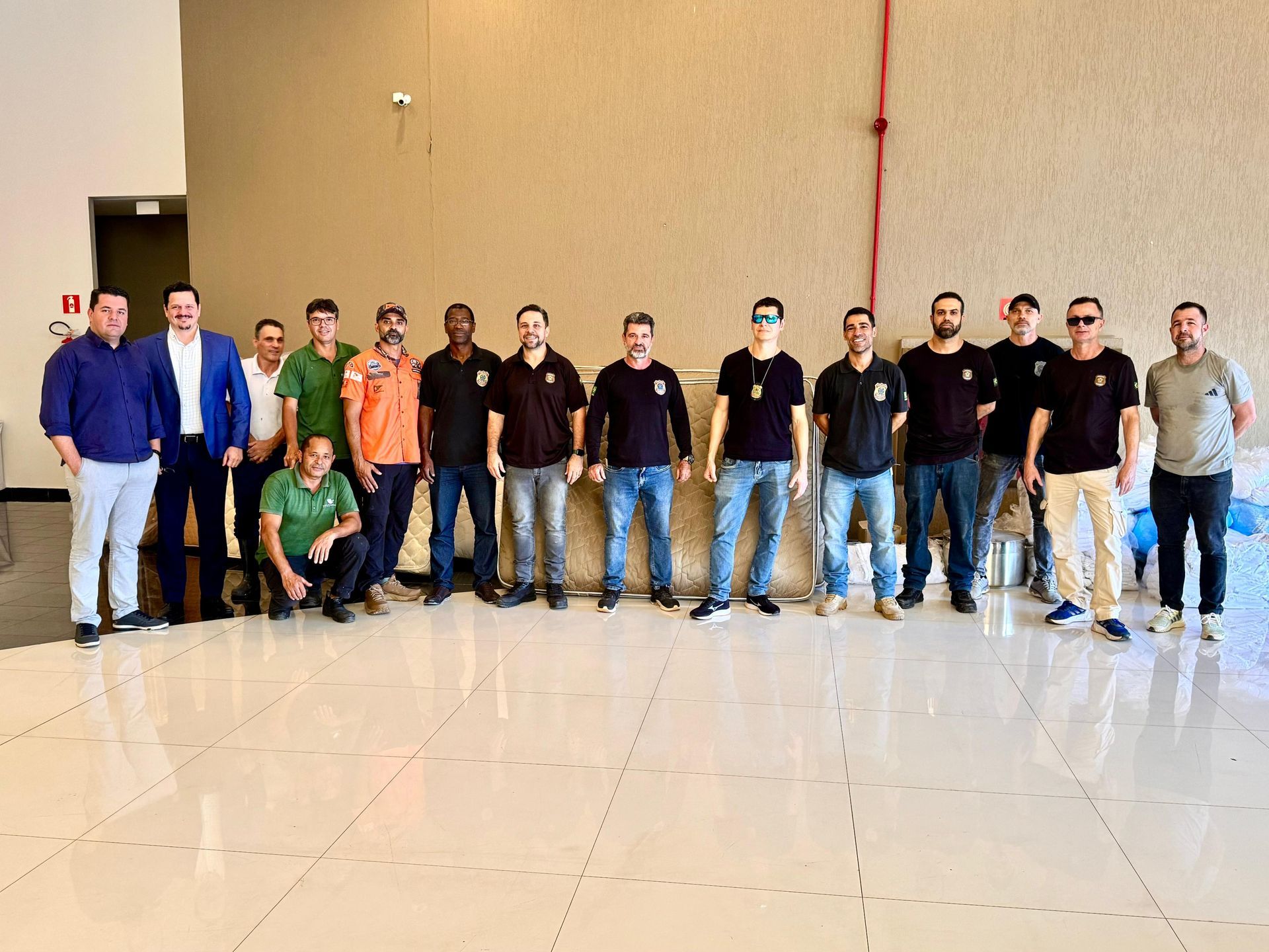 Um grupo de pessoas em fila num salão amplo e bem iluminado, com uma parede de cor neutra ao fundo.