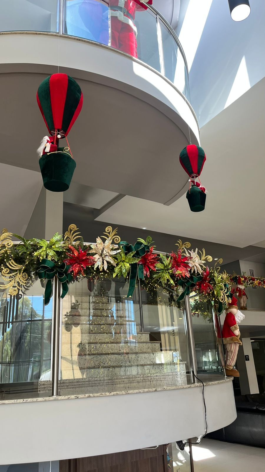 A decoração natalina festiva inclui balões de ar quente em miniatura, guirlandas de flores e uma figura do Papai Noel na grade de uma varanda.