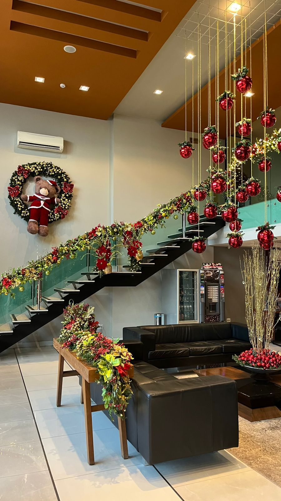Um saguão moderno decorado para o Natal, com uma grande escadaria adornada com enfeites vermelhos e uma guirlanda festiva.