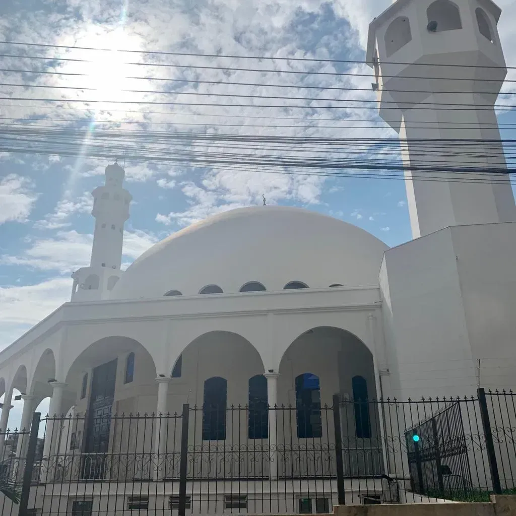 Mesquita branca com cúpula e minarete, céu azul brilhante.
