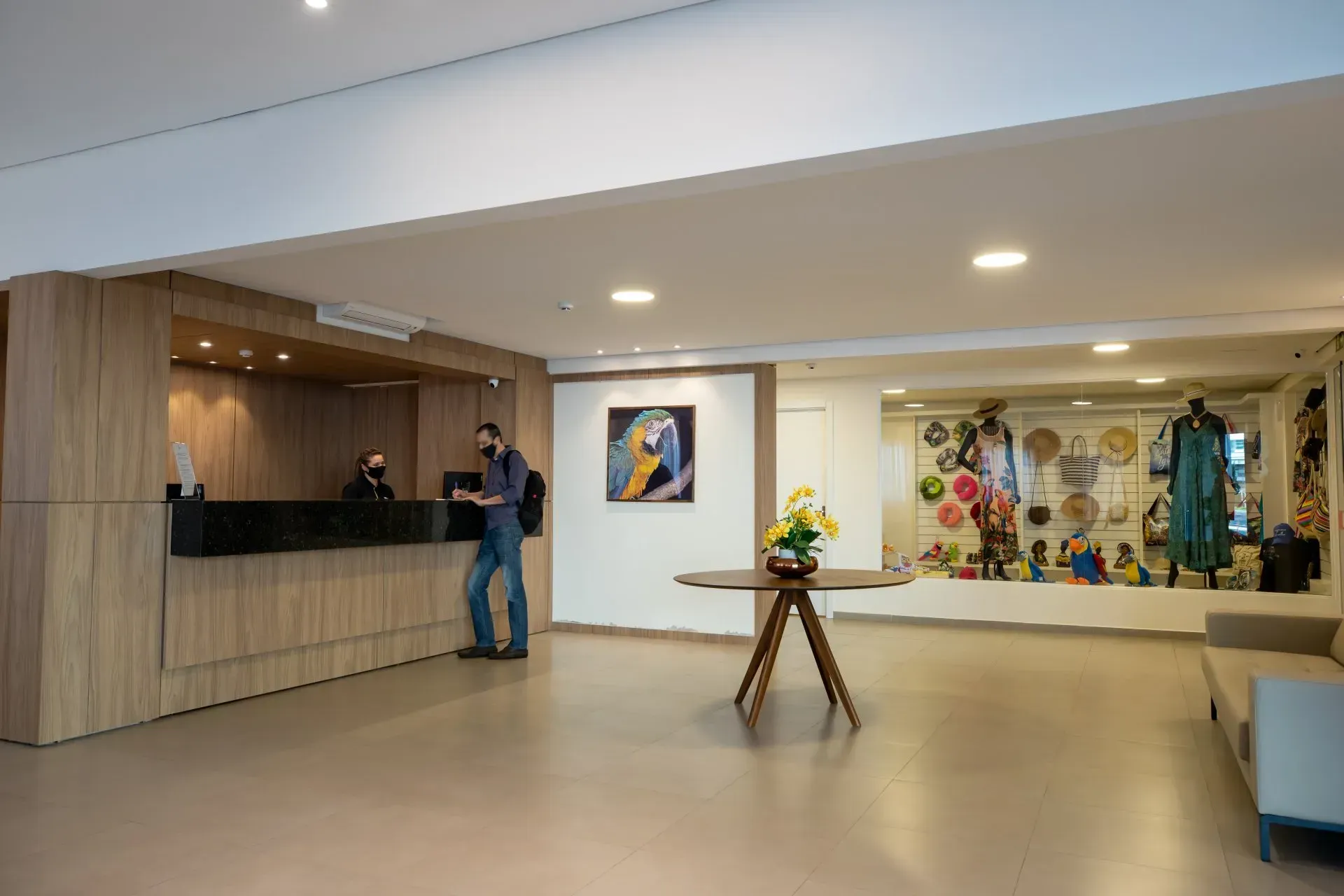 Saguão do hotel com recepção, check-in de hóspedes, vitrine de souvenirs e uma pintura.